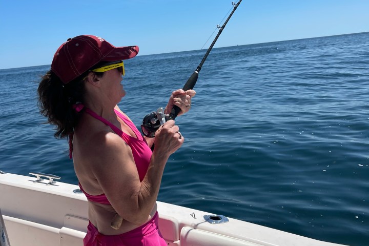 Person in pink outfit fishing on a boat in the ocean.