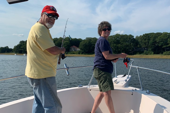Two people fishing on a boat under a clear blue sky.