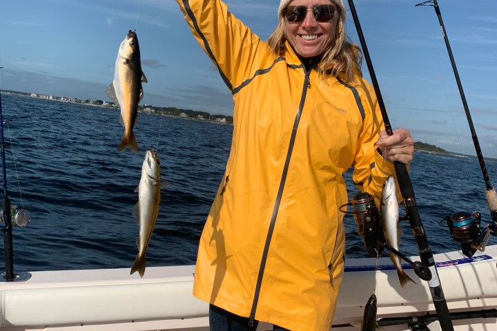 Smiling person in yellow jacket holding fish on a boat with fishing rods.