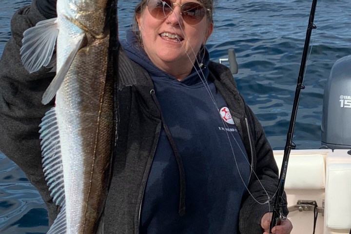 Person holding a large fish on a boat with ocean in the background, smiling.