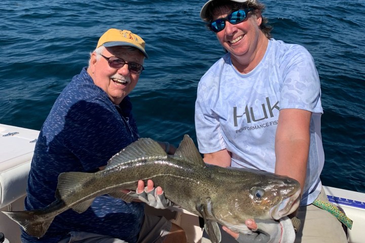Two people smiling while holding a large fish on a boat in the ocean.