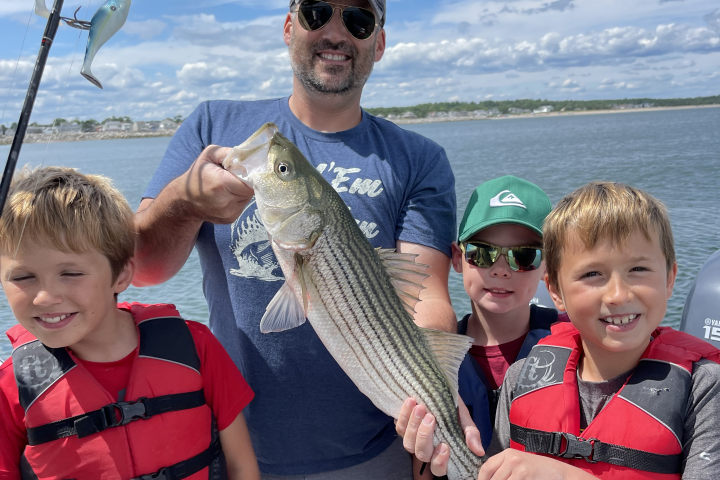 Man and three boys on a boat holding a large fish, all smiling.