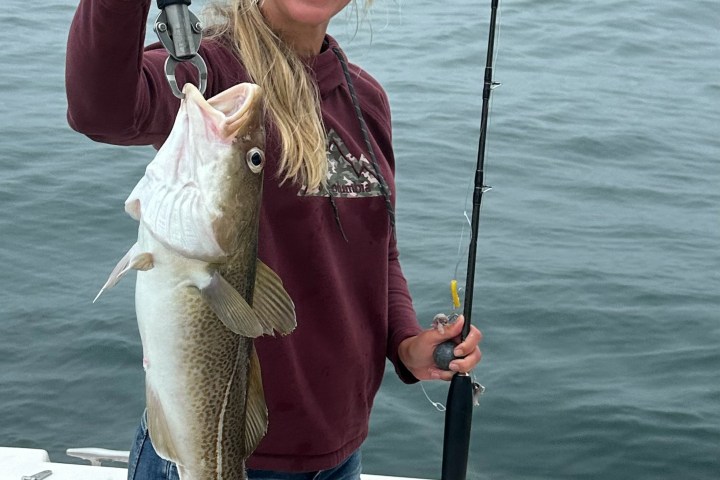 Smiling person on a boat holding a large fish and a fishing rod.