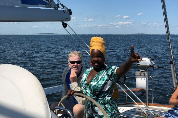 Two people steering a sailboat on a sunny day, one pointing upward.