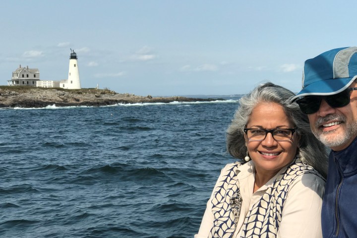 Smiling couple sitting by the sea with a lighthouse in the background.