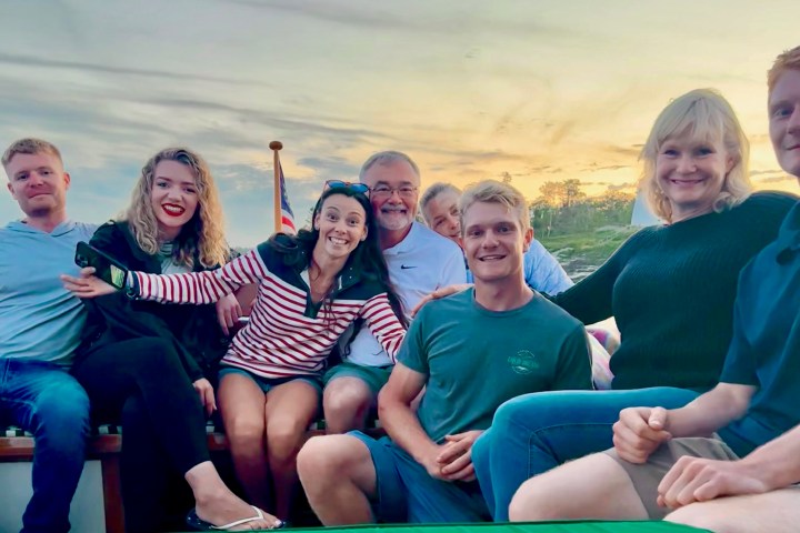 Group of seven people smiling on a boat during sunset.