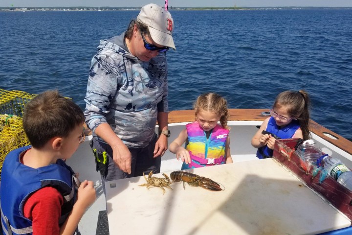 Children and adult on a boat examining a lobster on a table.