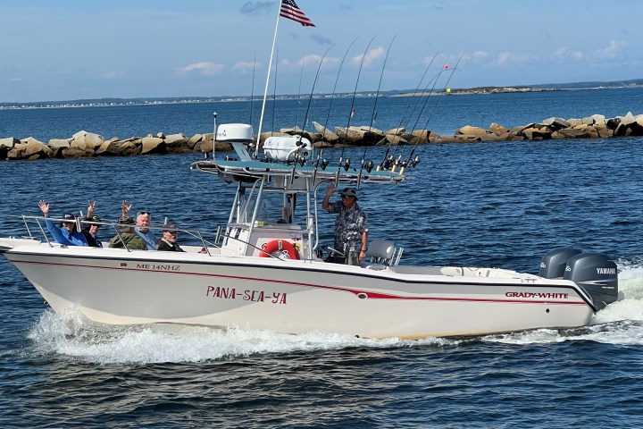 Motorboat with five people waving, American flag, and fishing rods on open water.
