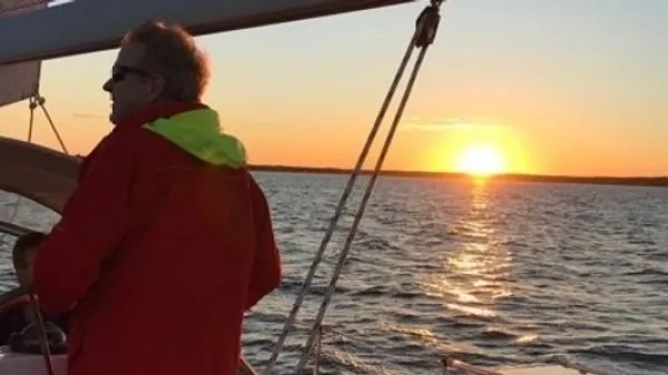 Person in red jacket sailing during sunset on calm water.