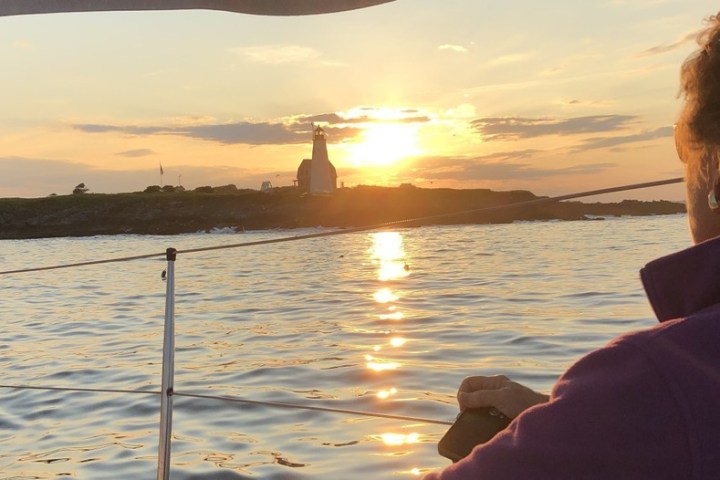 Person on boat watching sunset over water with island and lighthouse in background.
