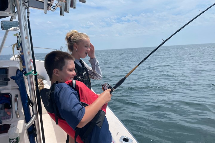 Two people fishing on a boat, one holding a fishing rod over the water.
