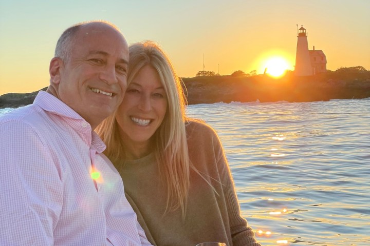 Smiling couple on a boat at sunset with a lighthouse in the background.